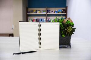 Notebook with lines and black pen on wooden table background with artificial flowers as decoration. photo