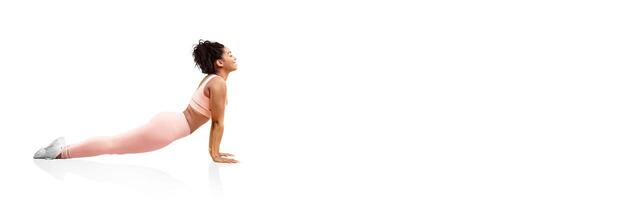 A person in pastel workout attire is executing a cobra pose, stretching their body while resting on a smooth surface. The bright studio adds a serene atmosphere to the practice. photo