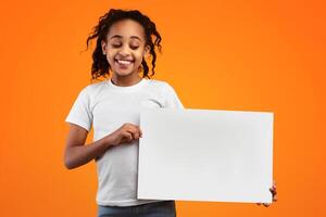 Banner For Advertising. Positive African American Girl Holding And Looking At Blank Square Paper Poster For Your Text And Smiling, Standing Isolated Over Yellow Studio Background, Free Copy Space photo