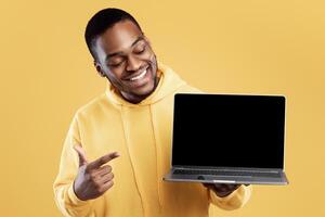 Black Young Man Showing Laptop Computer Blank Screen Advertising Great Website Posing Over Yellow Studio Background. Mockup For Advertisement. People And Gadgets, Internet And Technology Concept photo