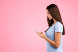People, Technology And Communication Concept. Side view portrait of smiling woman chatting on her cellphone, isolated over yellow studio background, free space. Young woman using smartphone photo