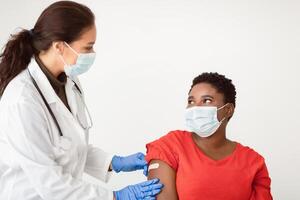 Antiviral Vaccination, immunization. African american female getting vaccine against Covid-19 for Coronavirus prevention. Medical worker sticking plaster bandage after injection on white background photo