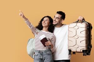 Travel Advertisement. Joyful Arab Couple With Suitcase And Passports Pointing Away At Copy Space On Yellow Background, Happy Middle Eastern Travellers Demonstrating Free Place For Ad, Panorama photo