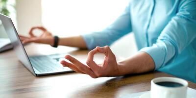 Unrecognizable Arab guy meditating in front of laptop pc, making gyan mudra with both hands, trying to keep calm at workplace, closeup. Stress management, work life balance concept photo