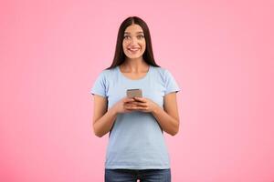 Chatting With Friends Online. Portrait of excited emotional lady using smartphone standing and posing isolated on yellow studio background, free space. Smiling woman looking at camera, holding gadget photo