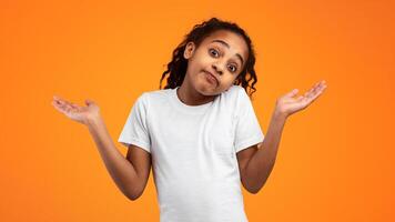 Pardon, I Don't Know. Portrait of Funny Young Black Girl Shrugging Shoulders Being At A Loss Posing Over Orange Background. Studio Shot. Puzzled student is clueless. I'm sorry, exuse me, can't decide photo