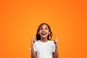 Check This. Portrait Of Excited Funny Black Young Girl Pointing With Two Fingers Up And Looking At Copy Space Above Her Head, Isolated On Yellow Background, Kid Demonstrating Free Place For Your Ad photo