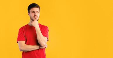 Pensive displeased young man thinking about question, touching chin and looking away at copy space, contemplating about something. Guy standing isolated over blue studio background photo