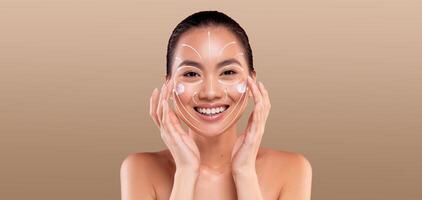 Asian woman enjoys her skincare routine, applying products while smiling in a peaceful, isolated setting. The focus is on her radiant skin and the joy of self-care amidst empty space. photo