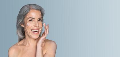 A woman is applying skincare products to her face with a joyful expression. She embraces self-care and beauty in a tranquil, minimalist environment with soft colors. photo