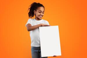 Banner For Advertising. Positive Black Girl Holding And Looking At Blank Vertical Paper Poster For Your Text And Smiling, Standing Isolated Over Yellow Studio Background, Free Copy Space Mockup photo