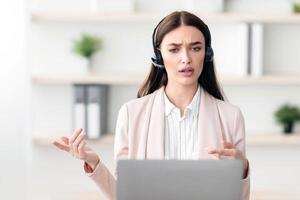 Professional Female Manager Making Call Talking With Client Sitting At Laptop And Solving Customer's Problems In Modern Office, Wearing Headset. Hotline Service Operator, Online Consultation photo