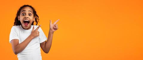 Check This. Portrait Of Excited Black Young Girl Pointing With Two Fingers Aside At Copy Space On Yellow Background, African American Kid Demonstrating Free Place For Your Design Or Advert, Banner photo