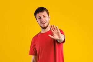 Keep Distance, Don't Stay Close To Me. Displeased young guy with disgusted facial expression raising hand, showing stop gesture with palm to camera, standing isolated over blue studio background photo