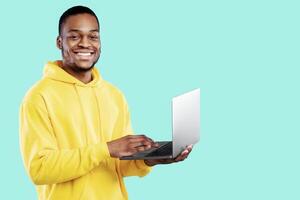 Happy African American Freelancer Guy With Laptop Posing Holding Computer Working Online And Browsing Internet Standing Over Blue Studio Background. Technology, Great Website Concept photo