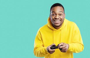 Gaming. Cheerful Black Guy Playing Videogame Holding Game Controller Smiling To Camera Standing Over Blue Background. Studio Shot Of Gamer Man Posing With Joystick photo