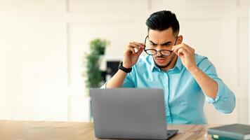 Irritated Arab businessman looking at laptop screen, having problem in online work at office. Young company employee with portable computer feeling stressed, experiencing business trouble photo