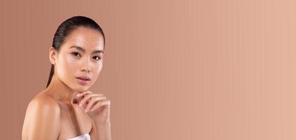 Asian woman applies a skincare product while relaxing and pampering herself in a minimalistic setting. The soft background enhances her natural beauty and care routine. photo