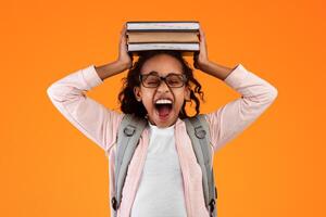 A Lot Of Homework. Portrait of tired black student girl putting and holding pile of academic books on her head and screaming, wearing eyeglasses and backpack, yellow color studio background photo