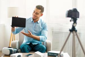 Arab guy vlogger making review of innovative tablet pc, using camera at home, mockup on touch pad screen. Popular influencer sharing info about new tech product with followers online photo