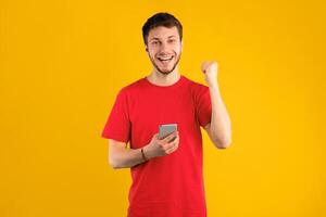 Big Win Online. Portrait Of Smiling Casual Young Guy Celebrating Success Using Mobile Phone. Happy Man Making Winner Gesture, Holding Gadget And Shaking Clenched Fist, Posing On Blue Studio Background photo