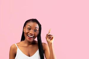Young black lady in summer clothes pointing upwards on pink studio background. Millennial African American woman experiencing AHA moment, having creative idea, gesturing eureka photo