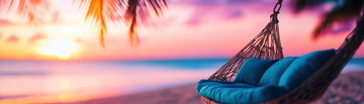 A blue hammock is hanging over the ocean, with a sunset in the background photo