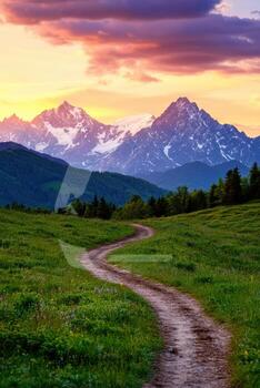 A road winds through a lush green field with mountains in the background photo