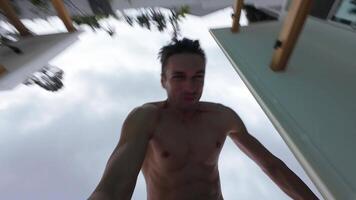 POV man jumps into resort pool filming himself during active leisure time during summer vacation. Selfie male millennial films himself doing flip into pool at villa. Active recreation concept video