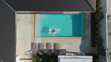 Top view man doing front flip into large swimming pool while relaxing at resort. Male dives into pool and swims in it while enjoying summer vacation at a luxury resort. Active summer vacation concept. video