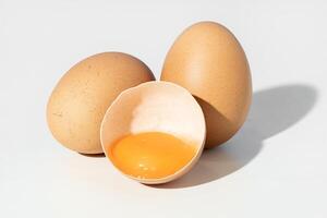 Studio shot of Two whole brown eggs and a broken eggshell containing an egg yolk isolated on white background photo