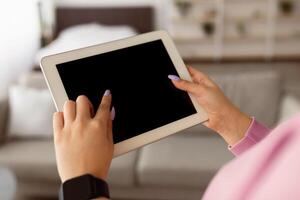 Closeup over the shoulder view of unrecognizable woman using tablet pc, mock up for design. Young lady with touch pad standing in living room indoors, touching screen with fingers, free copy space photo