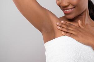 Hair Removal Concept. Unrecognizable Black Female Demonstrating Her Armpit With Smooth Skin, Smiling African American Woman Wrapped In Bath Towel Standing Over Grey Background, Copy Space photo
