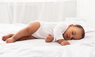 Cute Little Baby Sleeping Lying On Side In Bed In Bedroom At Home, With Eyes Closed. Peaceful Toddler Child Napping Resting During Daytime Sleep Indoors. Side-View Shot photo