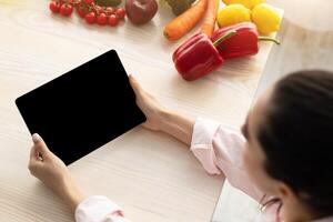 Above top high angle view of lady holding and using digital tablet with black empty isolated screen for mock up design, having breakfast drinking coffee in the morning, watching , free copy space photo