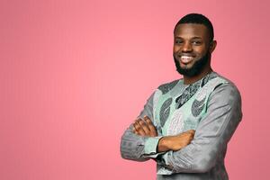 Confident smiling african american guy in bright traditional t-shirt over pink studio background, copy space. Handsome black man posing with arms crossed, free space for text or advertisement photo