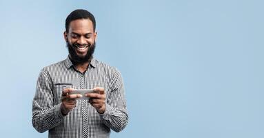 Gaming Concept. Smiling black guy using cellphone, browsing internet and chatting, turquoise wall, copyspace photo