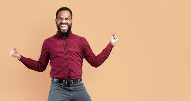 Funny portrait on joyful black man jumping with clenched fists isolated on yellow studio background, full length photo