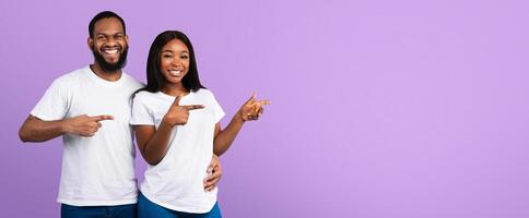 Cool Offer. Portrait Of Smiling African American Young Couple PointingFingers Aside At Copy Space On Blue Background, Man Embracing Woman And Looking At Camera, Presenting Free Place For Your Advert photo