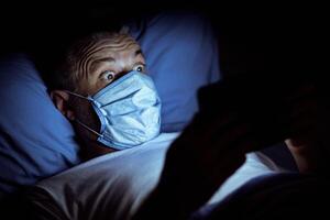 Self-Quarantine Anxiety. Shocked Man Reading News On Tablet Computer Overnight Lying In Bed At Home. Panorama, Low Light photo