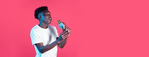 A young black man stands in front of a bright pink background, passionately singing into a microphone. His energetic expression conveys a deep connection to the music he is performing. photo