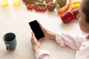 Breakfast Concept. Over the shoulder above view of young female holding in hand device with black empty screen for mock up design, checking email or browsing internet sitting at dinner table photo