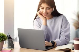 People And Modern Technology Concept. Portrait of smiling woman in wireless headphones sitting at desk, using laptop and watching tutorial, lecture or webinar, studying online at home photo