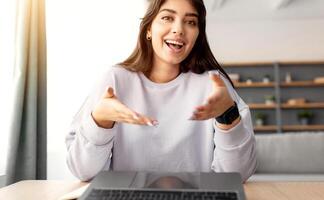 Online Call. Portrait of smiling young lady having virtual conference with friends, family or colleagues using computer, talking and gesturing to webcam, sitting at desk at home office photo