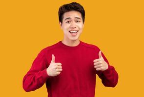 Everything Is Fine. Portrait of happy asian man showing thumbs up, doing approval gesture with fingers and both hands, smiling, showing that he is good, isolated over orange studio background photo