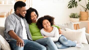 Modern African American Family With Little Daughter Spending Time At Home Together, Relaxing On Couch And Cuddling photo
