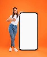Mobile Offer. Happy woman leaning on huge cellphone with blank white screen, showing thumb up gesture, recommending great new app or website for phone, offering space for ad, mock up, full body length photo