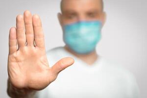 Stop Coronavirus. Unrecognizable Man In Medical Mask Gesturing Stop Standing Over Gray Background In Studio. Panorama, Selective Focus photo
