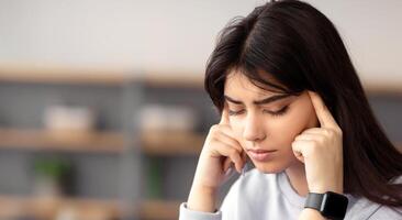 Fatigue From Work. Tired young woman feeling headache or stress, touching and massaging her temples. Female working on laptop, trying to learn and study, sitting at desk and using computer photo