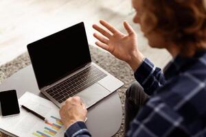 Distance Communication. Guy Making Call On Laptop With Empty Screen Communicating Online At Home, Back View. Unrecognizable Freelancer Talking To Computer Webcam. Selective Focus, High-Angle photo